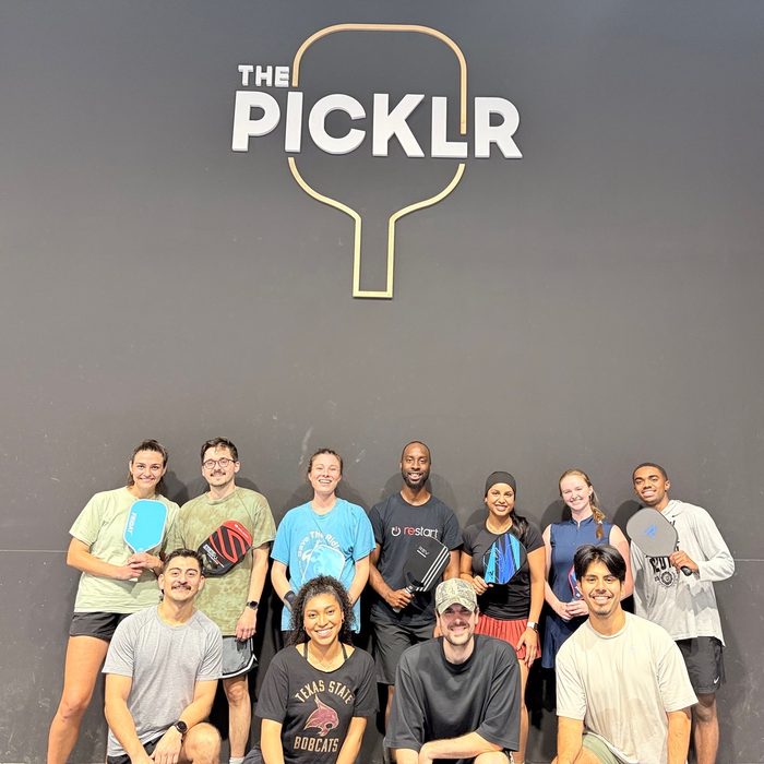 The pickleball league gathered for a group photograph under the club sign, paddles in hand