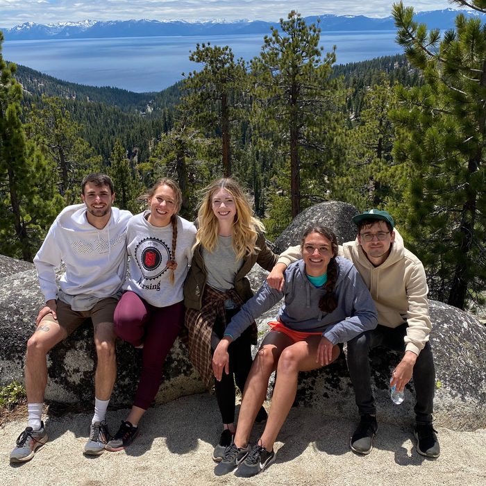 Five friends sitting together on a boulder among the pines, mountains and a lake behind them